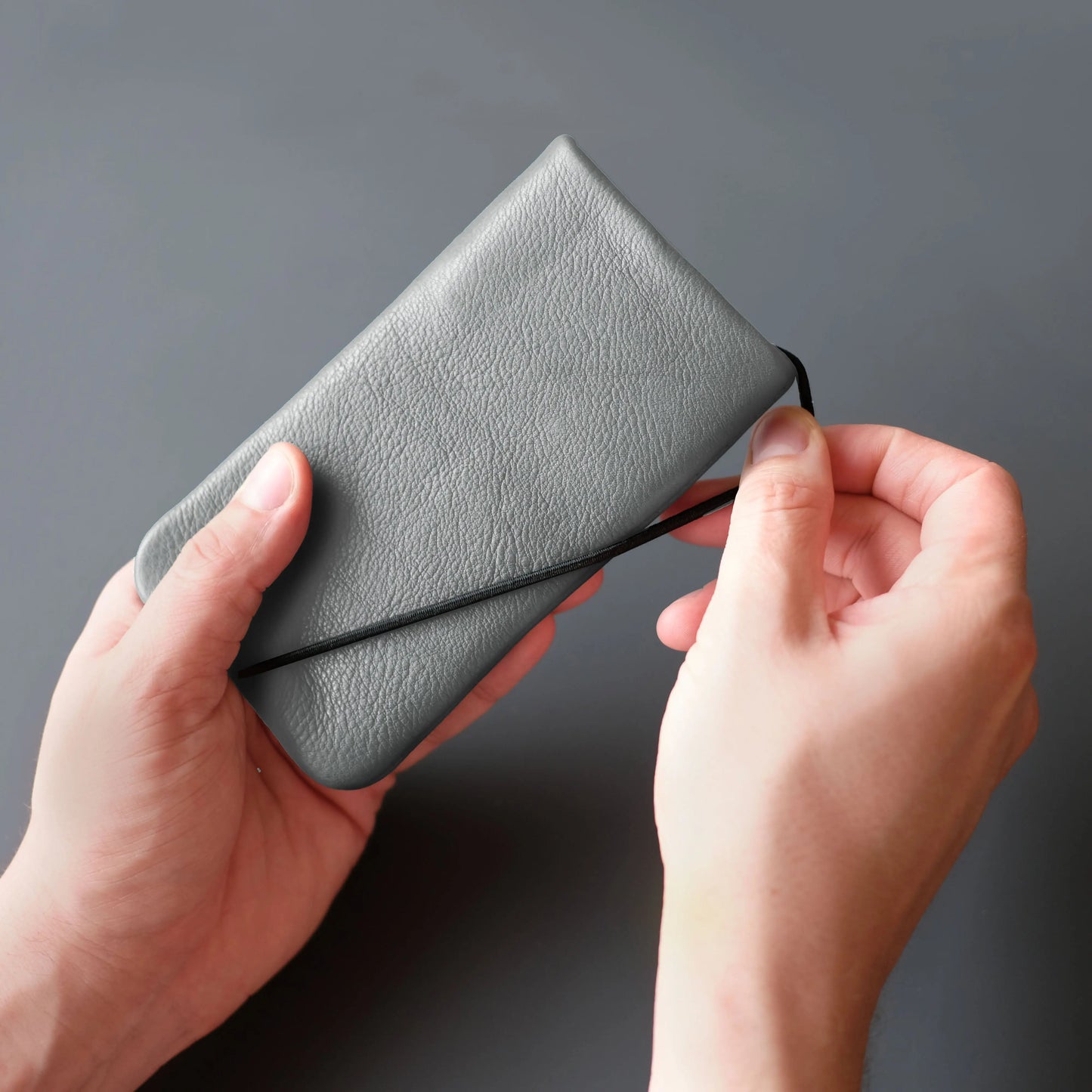 graue Lederhülle für Smartphones wird mit dem schwarzem Gummiband geschlossen