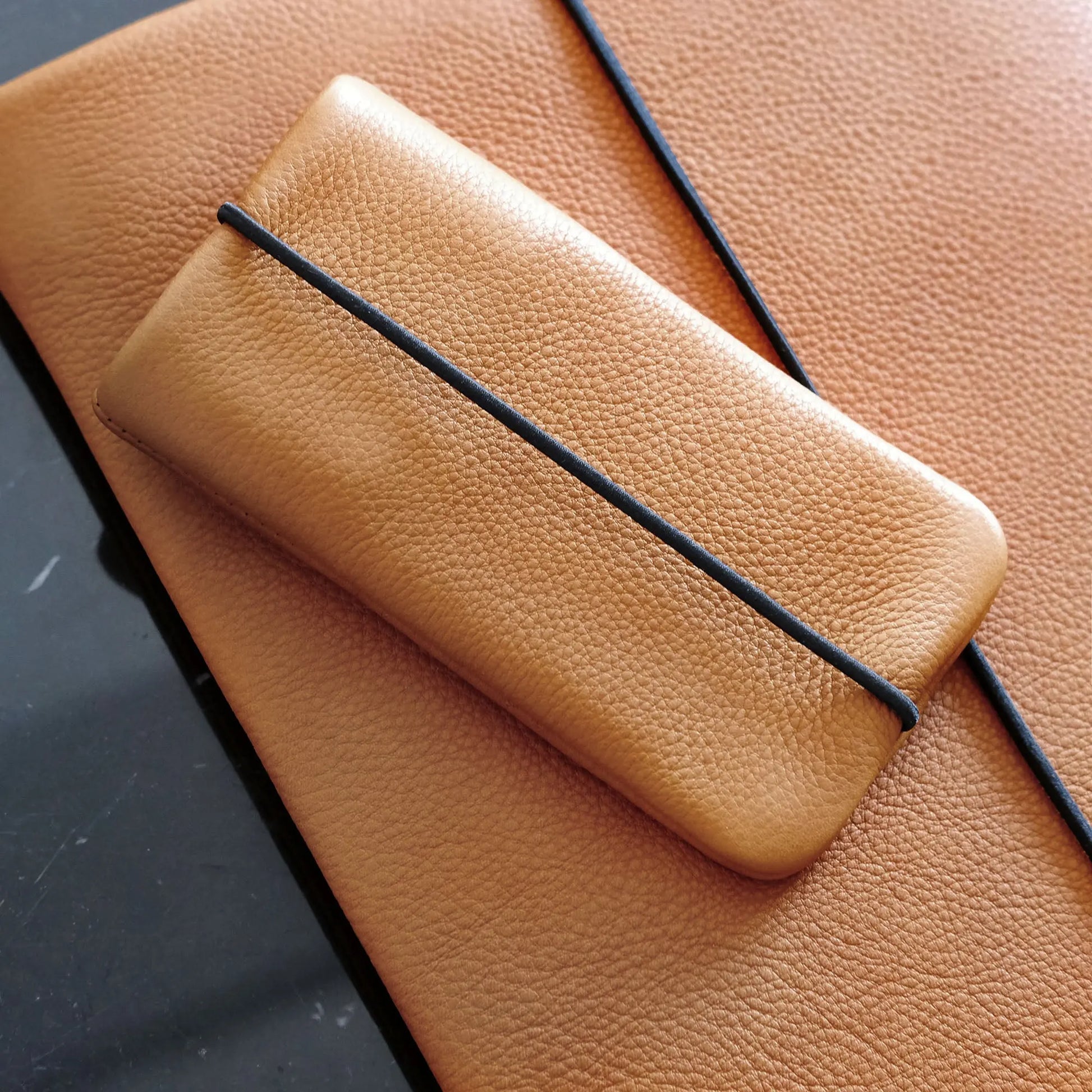 Handyhülle aus Leder in orange liegt auf passender Notebookhülle aus Leder