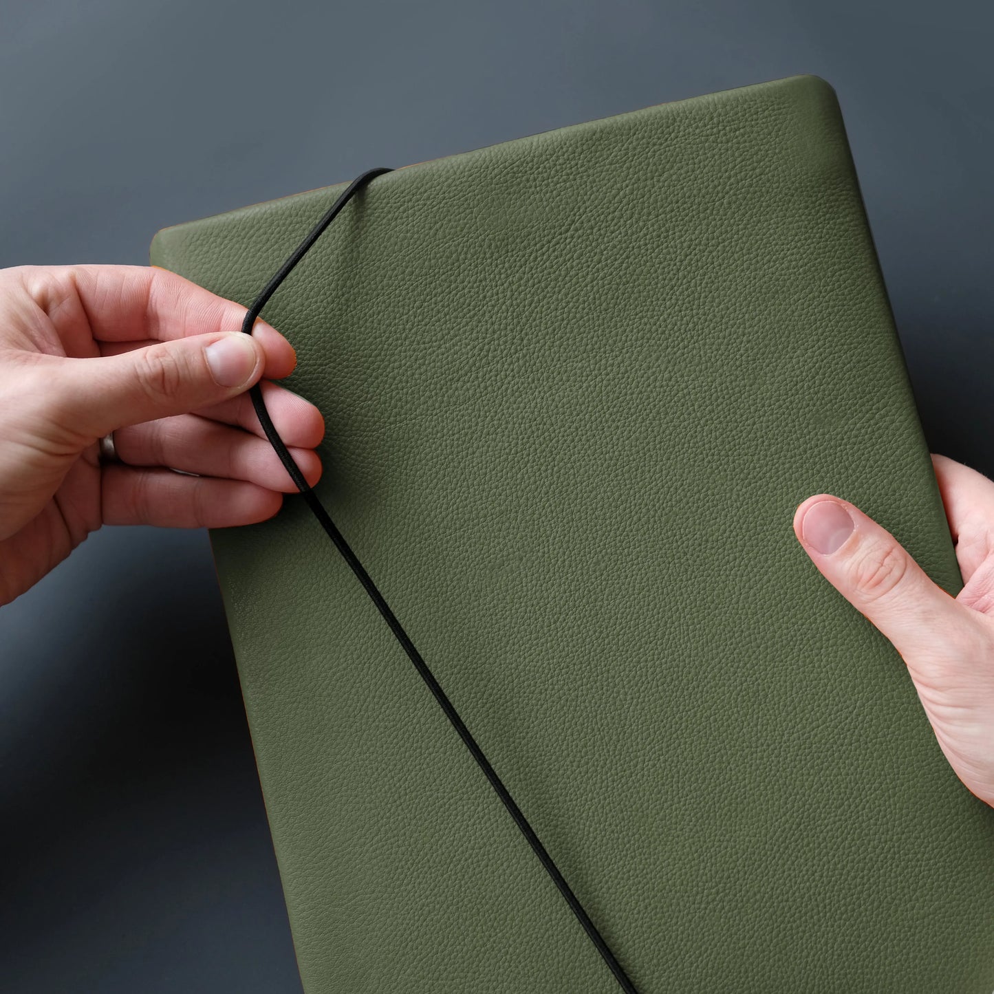 iPadcase aus khakifarbenem Leder, das von zwei Händen mit dem Verschussgummi geschlossen wird.