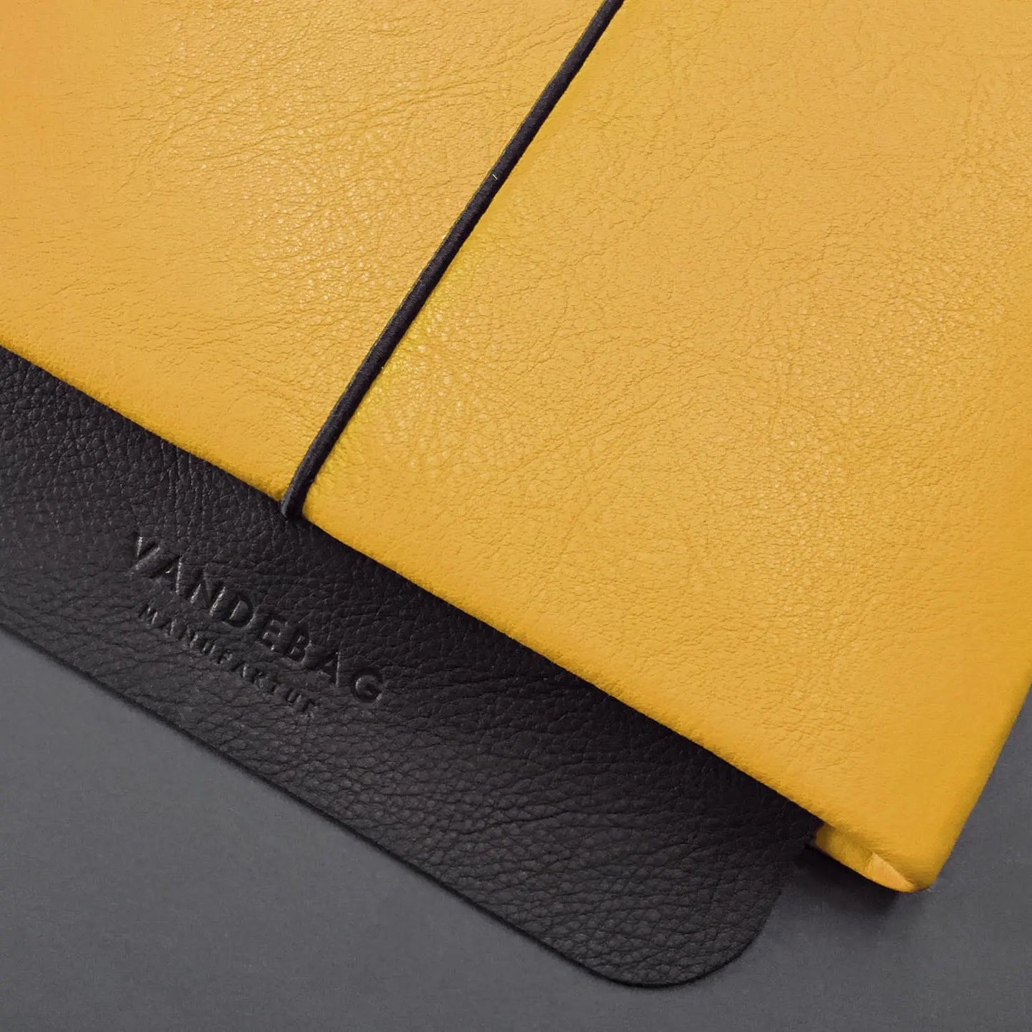 Lederhülle für Tablets in gelb mit Verschlussklappe aus schwazem Leder in die "Vandebag" eingeprägt ist.