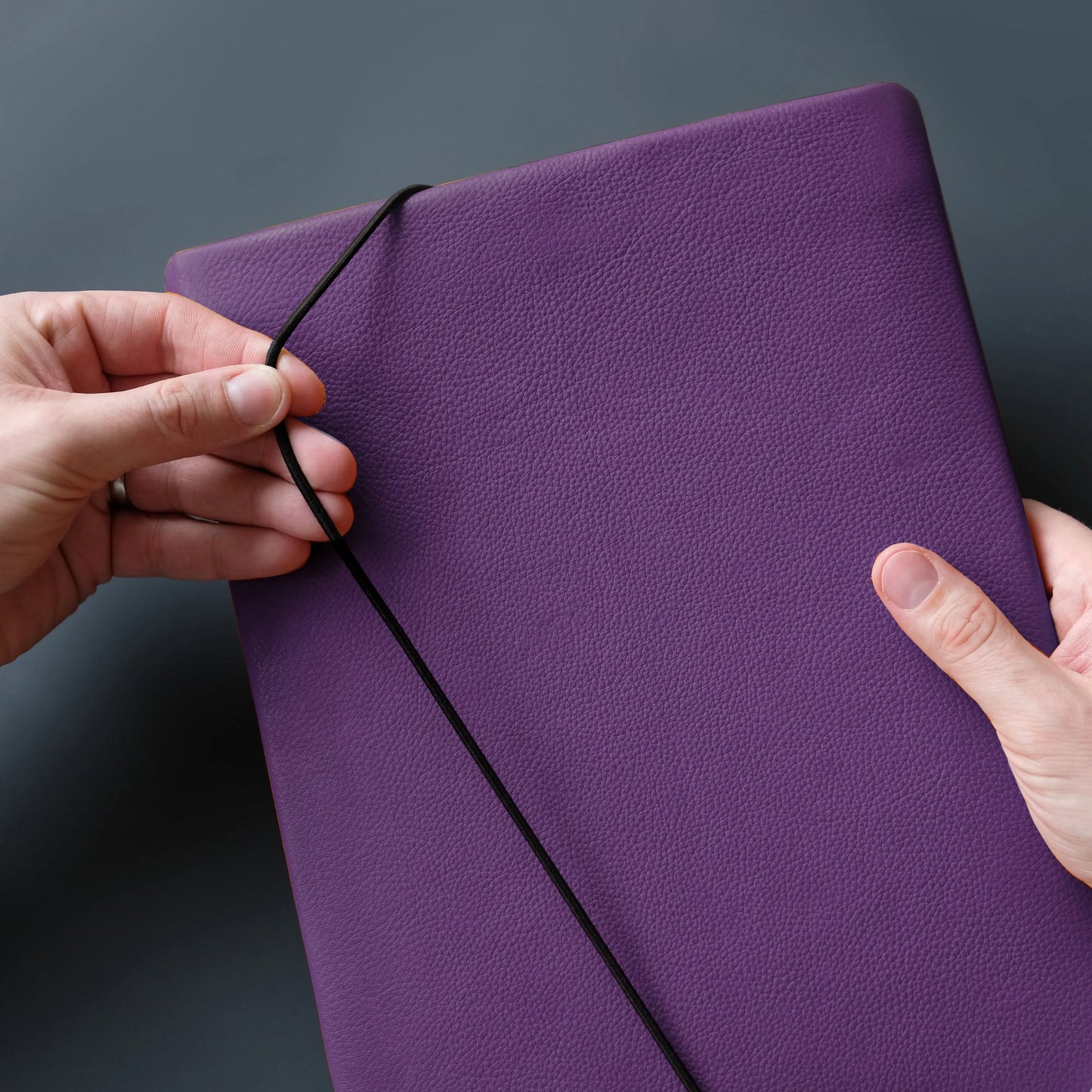lilafarbenes Tabletcase aus Leder, das von zwei Händen mit dem Verschlussgummi geschlossen wird.
