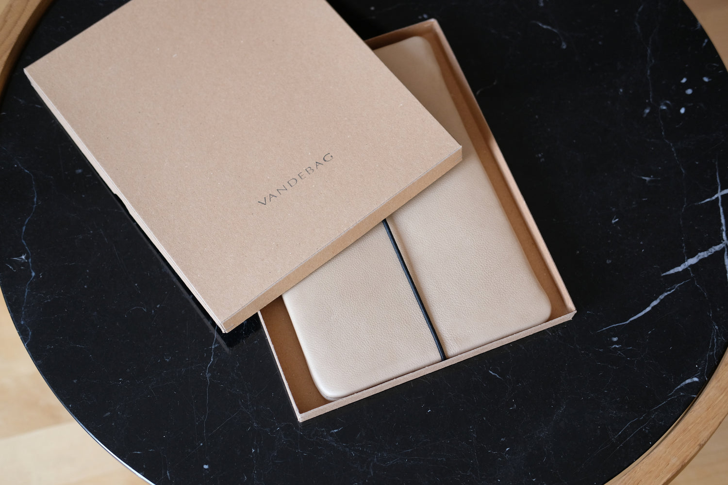 maßgefertigte Tablet Hülle aus beigem Leder liegt in einem braunen Produktkarton