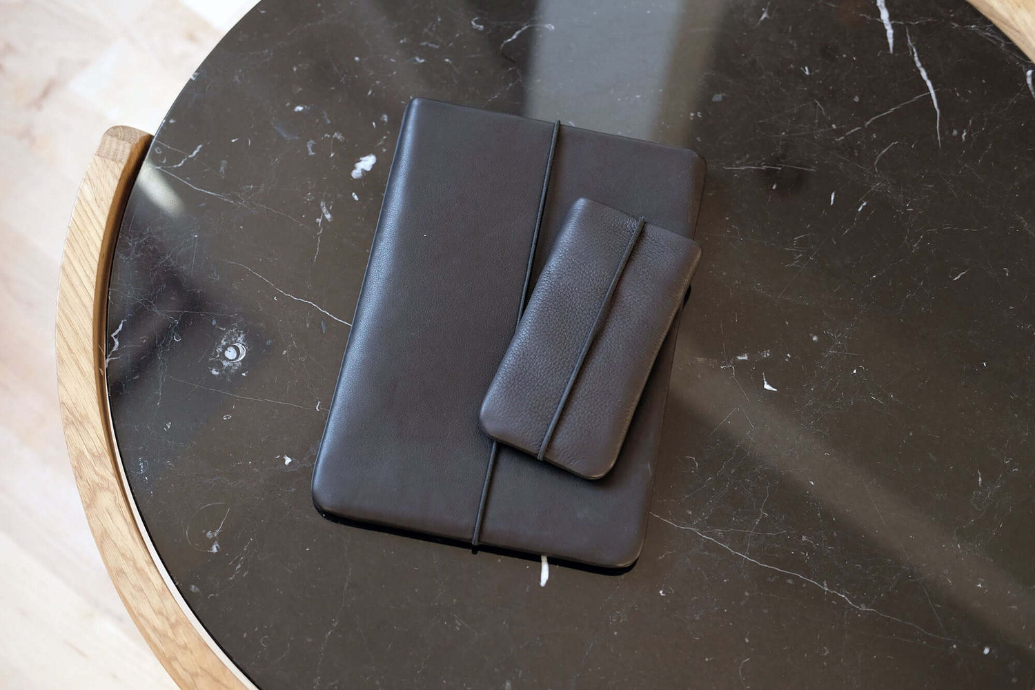 iPhoneHülle aus schwarzem Leder liegt auf schwarzer Tablethülle auf einem schwarzen Tisch 