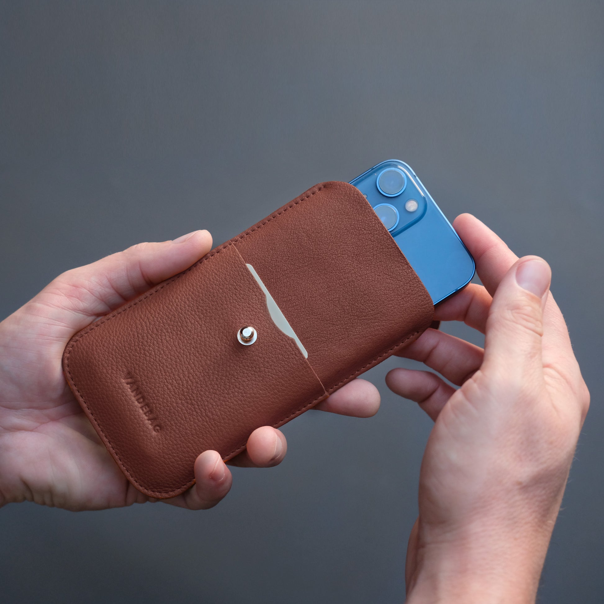 Hand schiebt iPhone in eine braune Handyhülle aus Leder