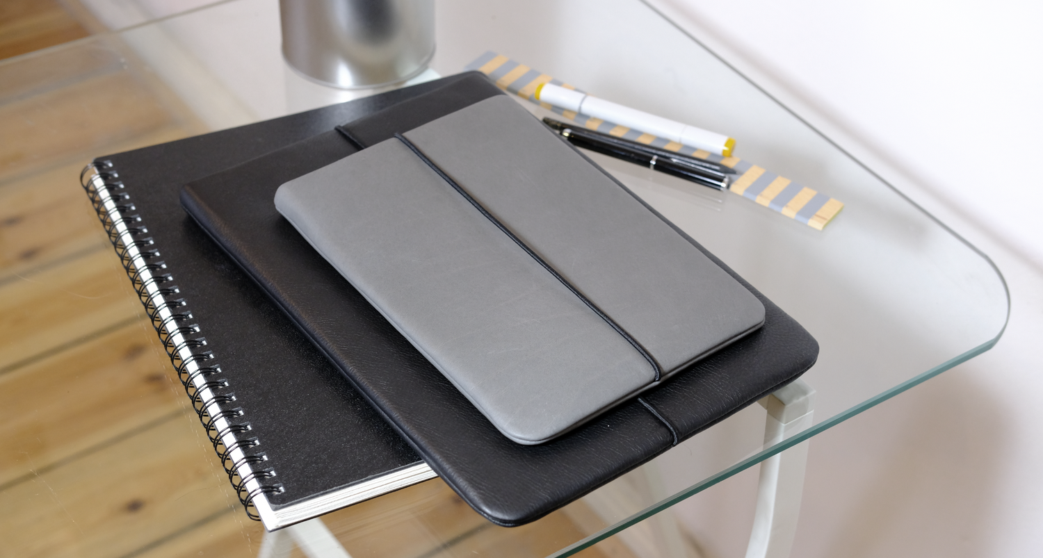 Tablet Hülle grauem Leder und Laptop Hülle aus schwarzem Leder liegen auf einem Notizbuch