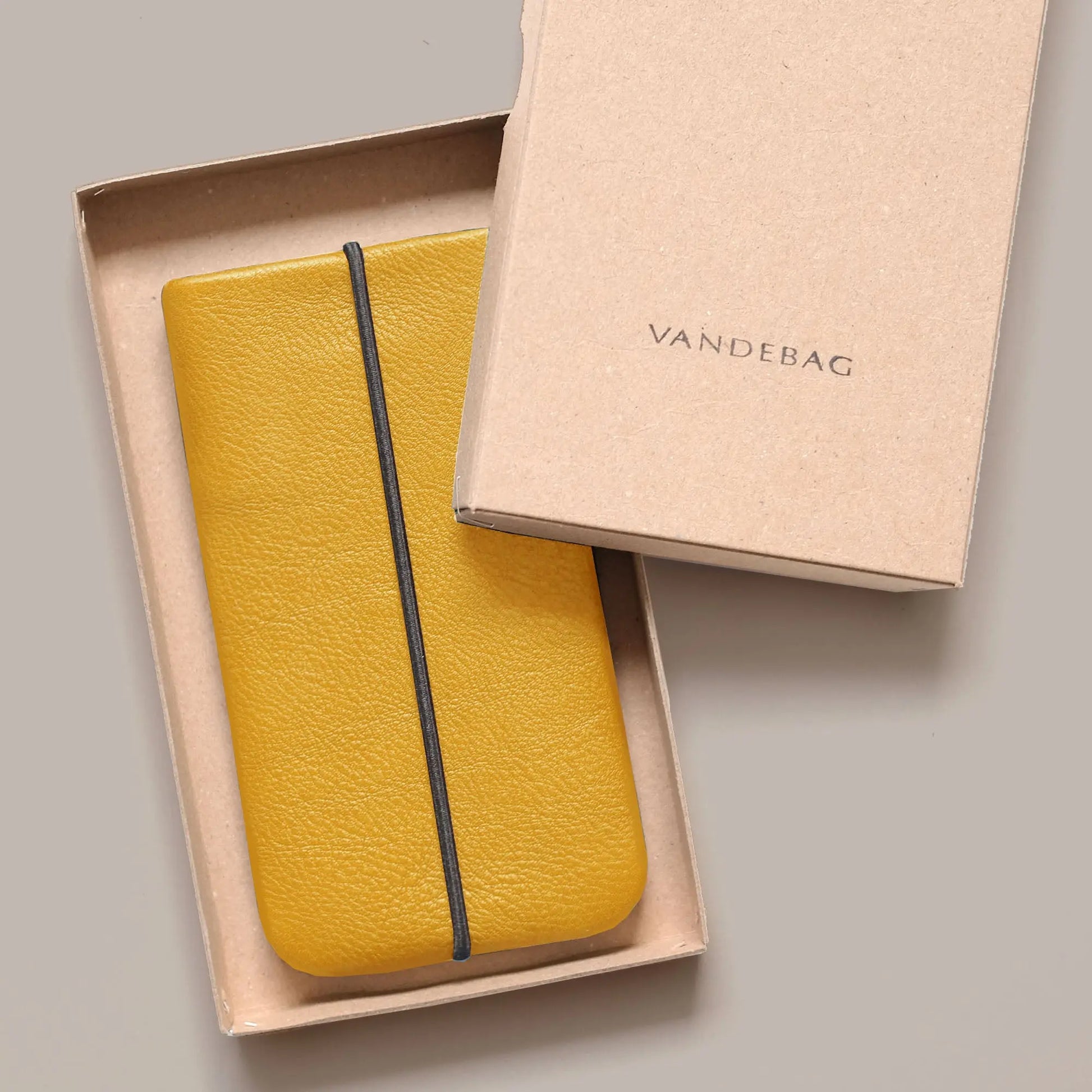 iPhonehülle aus gelbem Leder liegt in einer Produktbox aus Karton mit der Aufschrift Vandebag