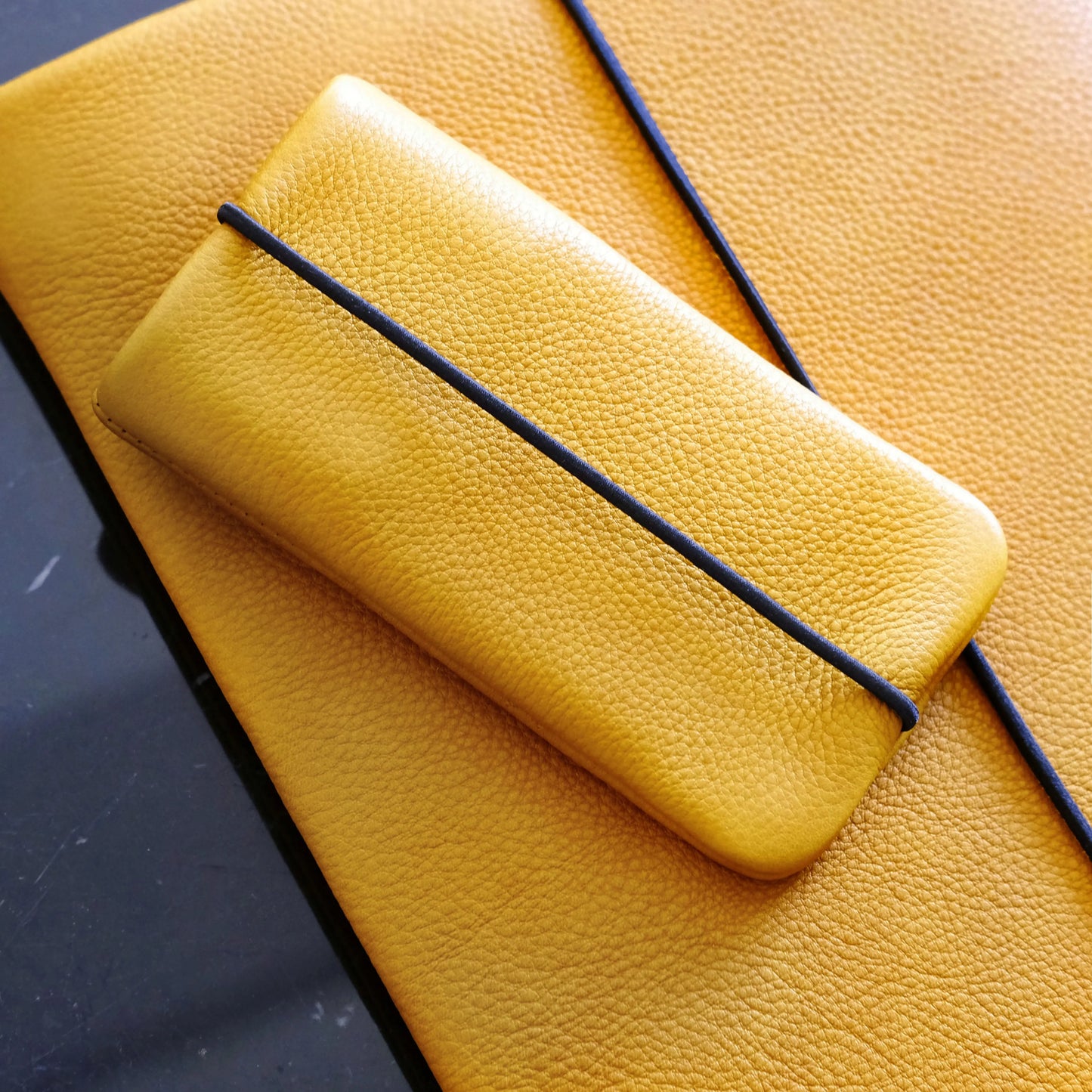 Handyhülle aus gelbem Leder liegt auf einer gelben Macbookhülle aus Leder