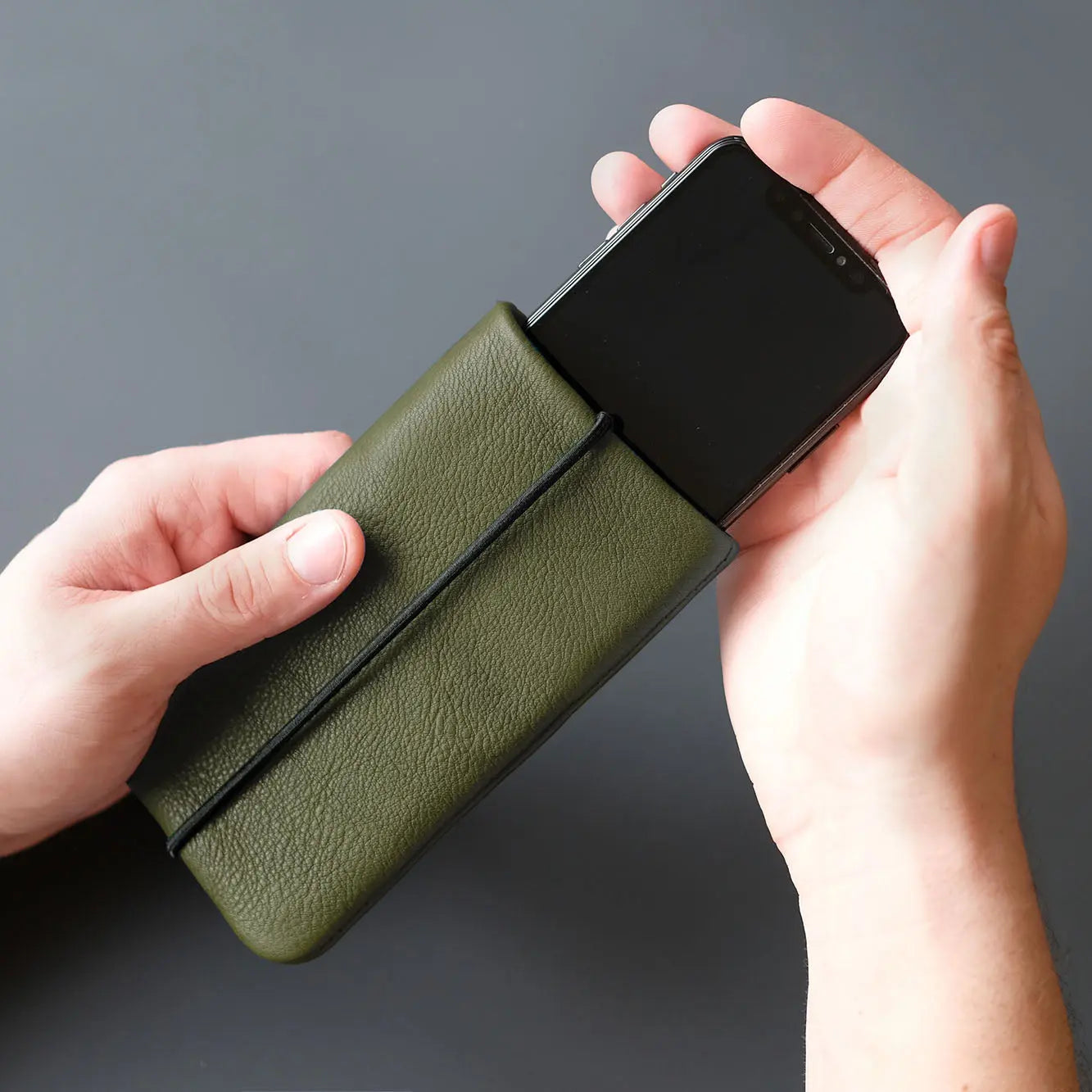 Smartphone wir in eine olivgrüne Lederhülle gesteckt