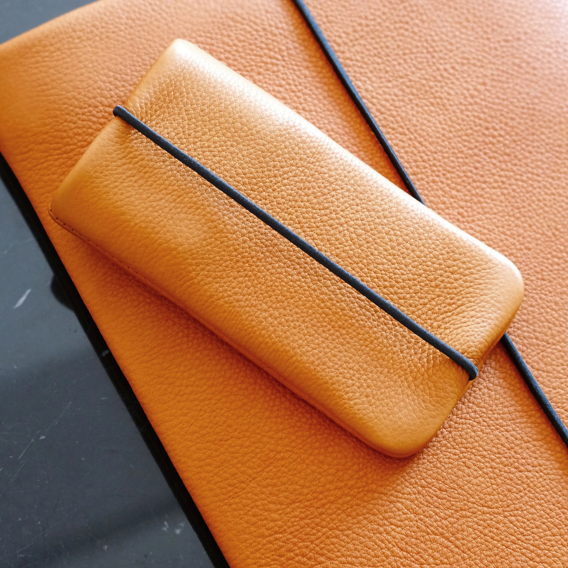 orangefarbene Lederhülle für iPhones liegt auf passender Leder-Macbookhülle