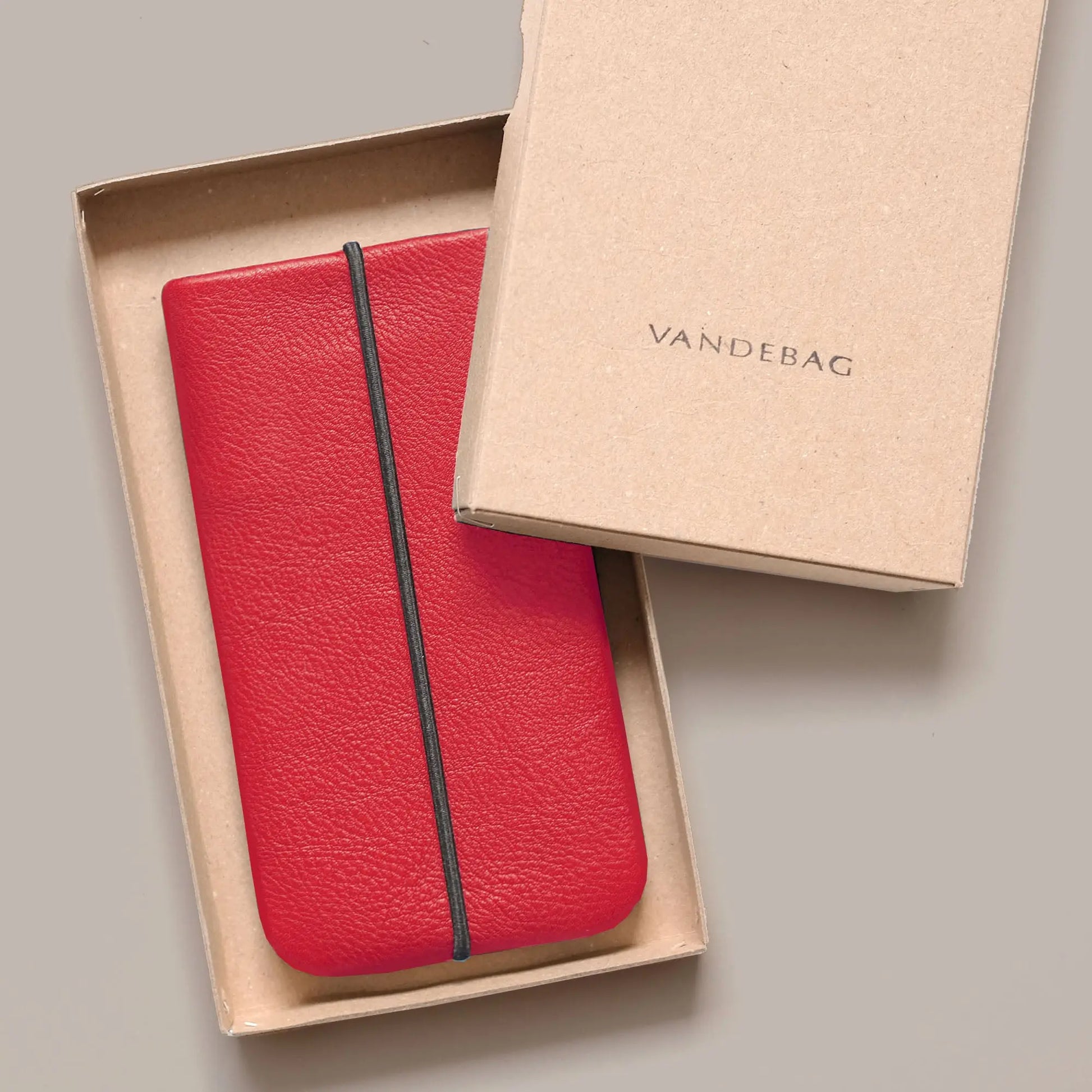 Smartphonehülle aus rotem Rindsleder liegt in Geschenkbox mit Aufschrift Vandebag
