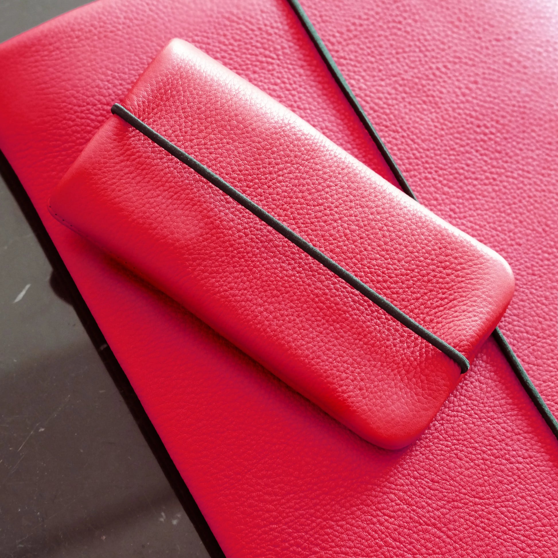 rote Lederhülle für Handys mit schwarzem Gummiband liegt auf passender Notebookhülle aus Leder