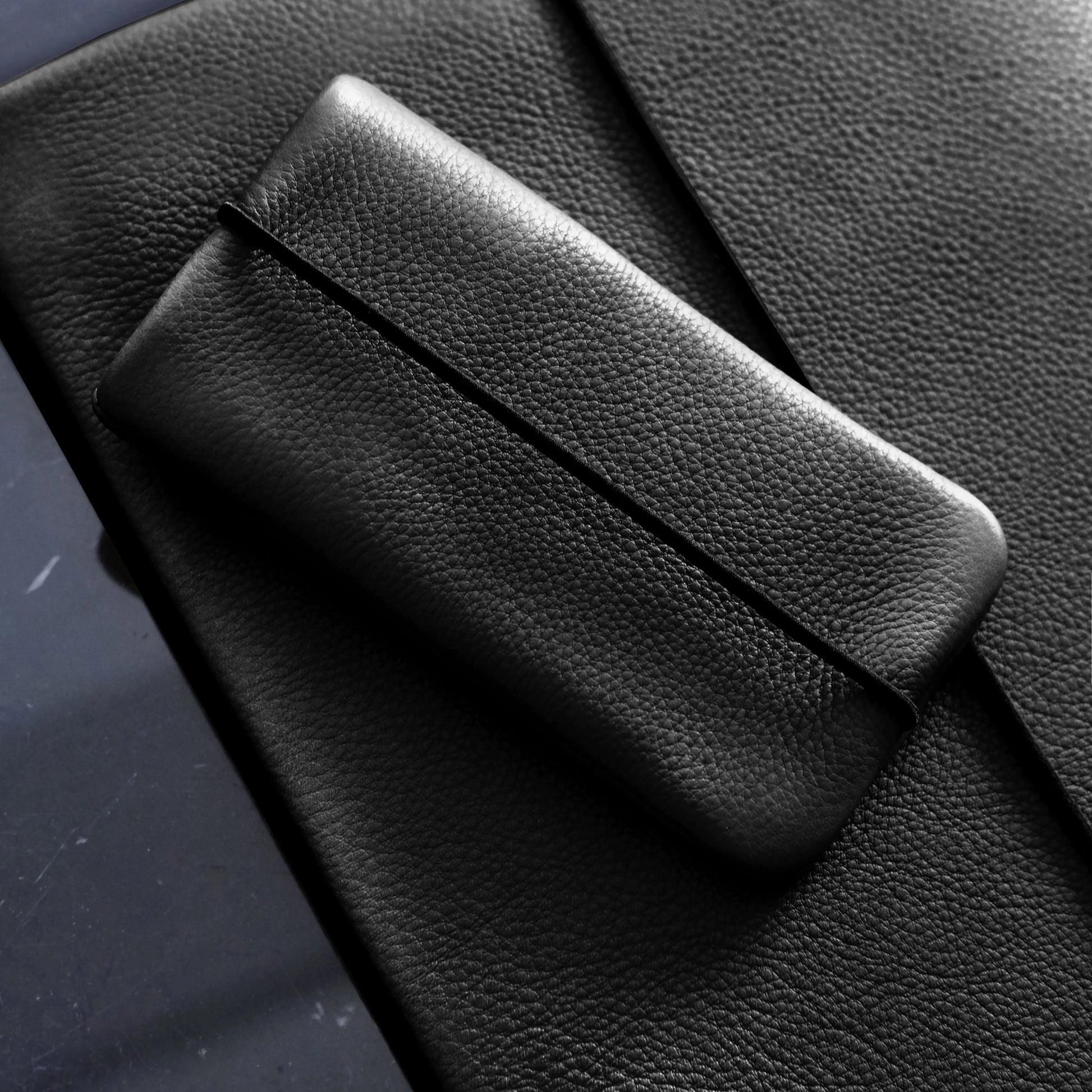 schwarze Lederhülle für Smartphones liegt auf einer schwarzen Macbookhülle aus Leder