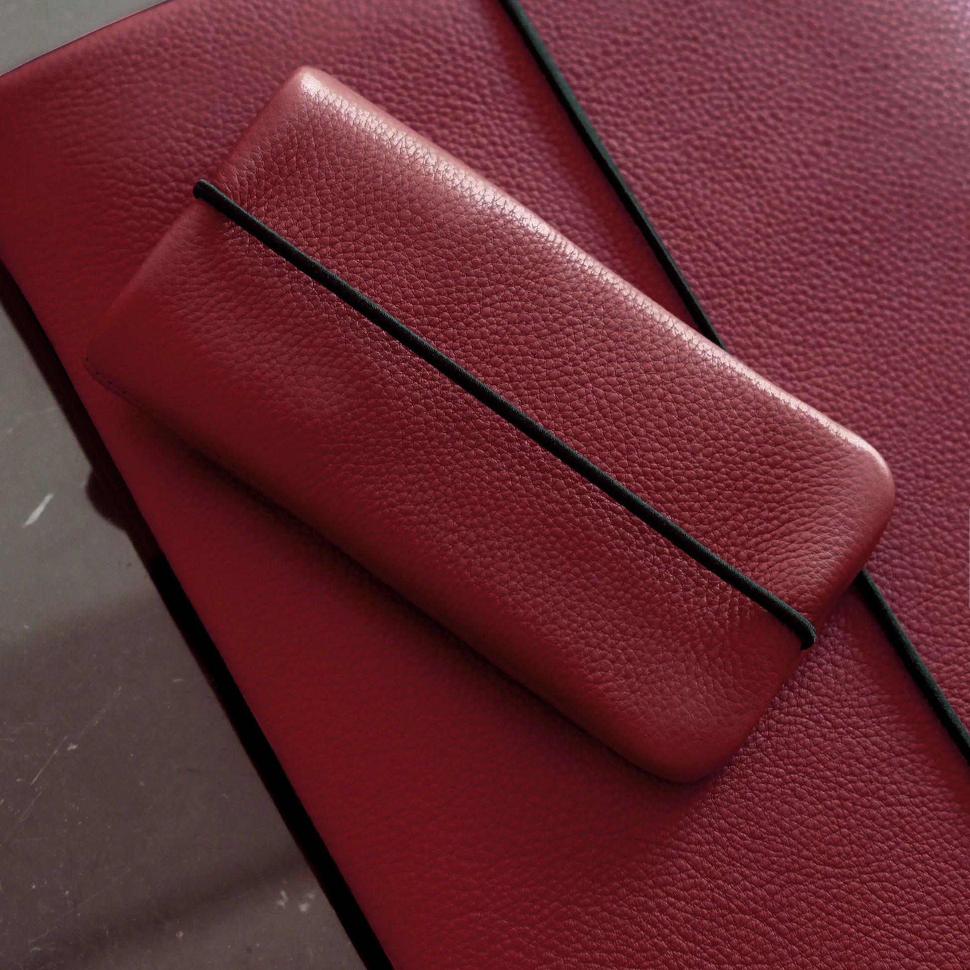 iPhonehülle aus dunkelrotem Leder liegt auf einer Macbookhülle aus dunkelrotem Leder