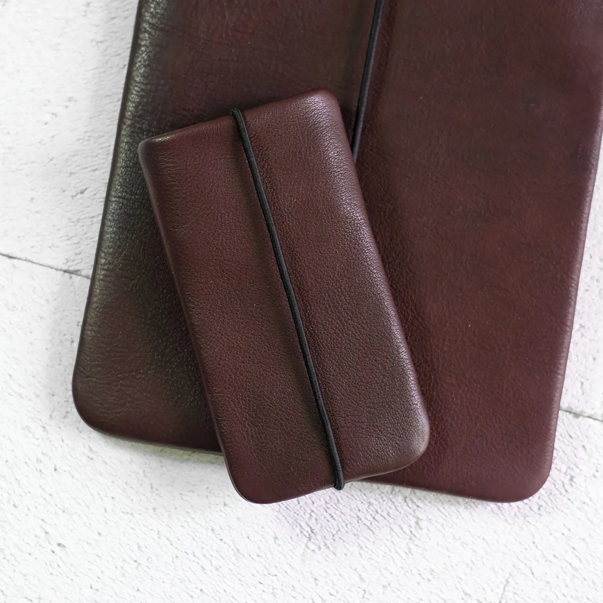 schokobraune Smartphonehülle aus Leder liegt auf einer Notebookhülle aus schokobraunem Leder