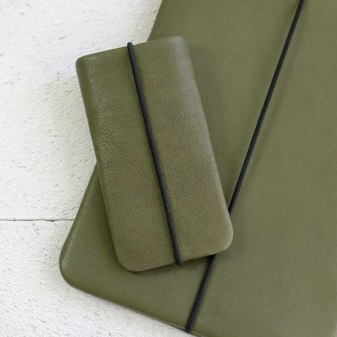 olivgrüne iPhonehülle liegt auf einer passenden Notebooktasche
