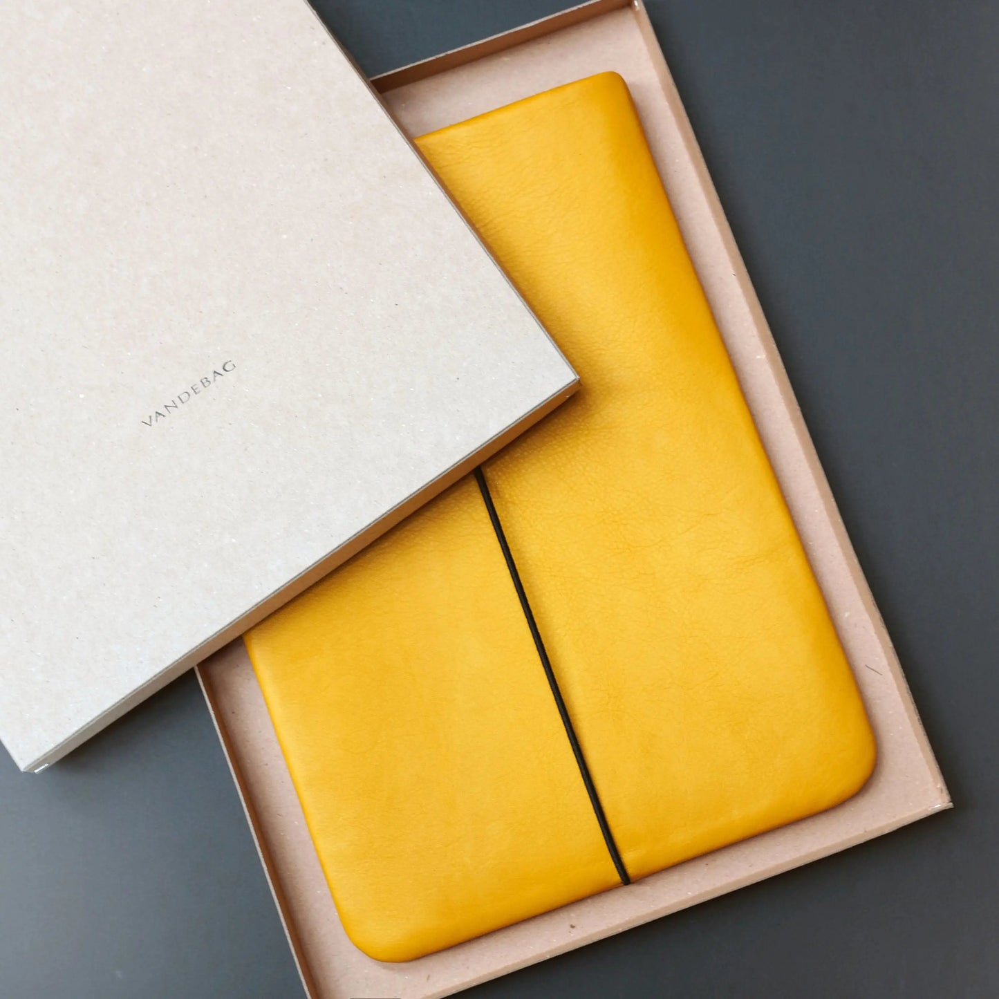 iPadhülle aus Leder in gelb, das in einem Produkkarton aus recycelter Pappe liegt