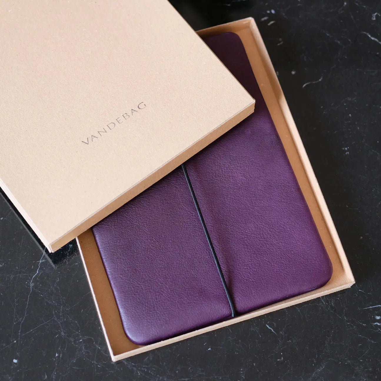 iPadhülle aus lila Nappaleder liegt in einem Geschenkkarton auf einem schwarzen Marmortisch