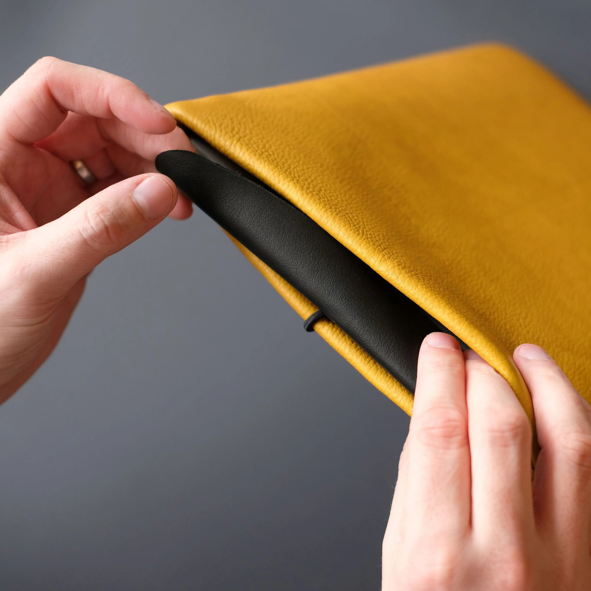 gelbe Lederhülle für iPads, das von zwei Händen mit der schwarzen Lederklappe geschlossen wird.