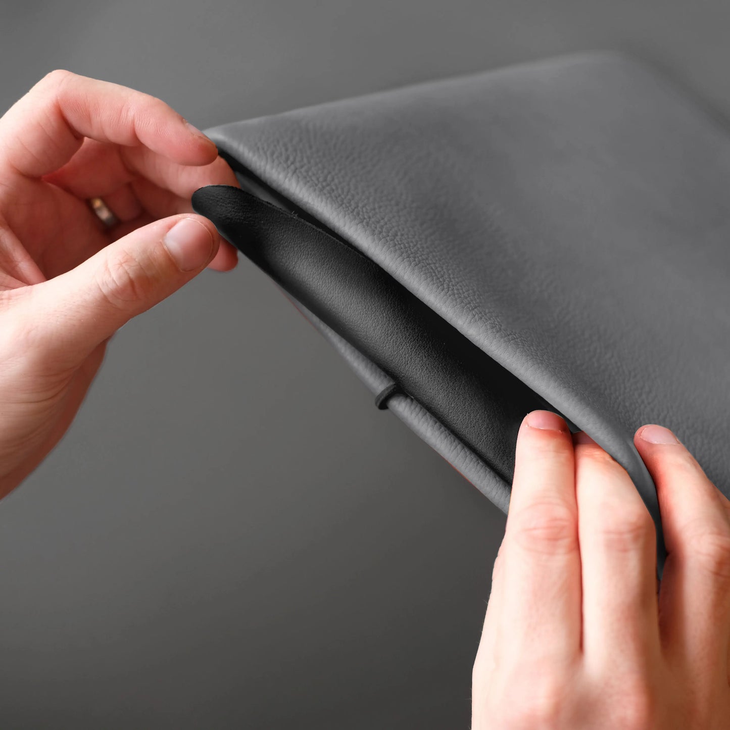 iPad Hülle aus grauem Nappaleder, das geschlossen mit der schwarzen Lederklappe von zwei Händen geschlossen wird.