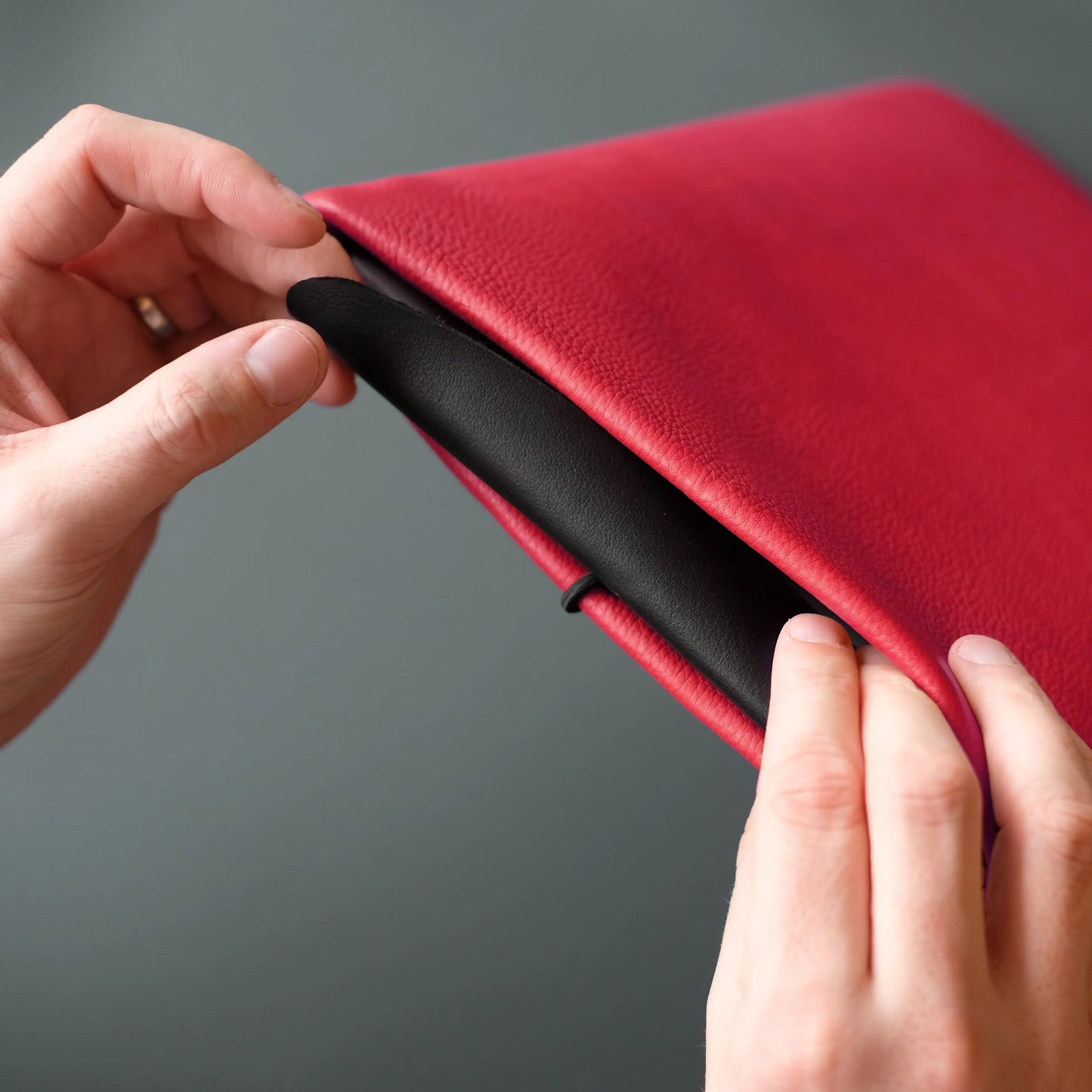 schwarze Lederklappe wird in rote Notebook Hülle aus Leder gesteckt