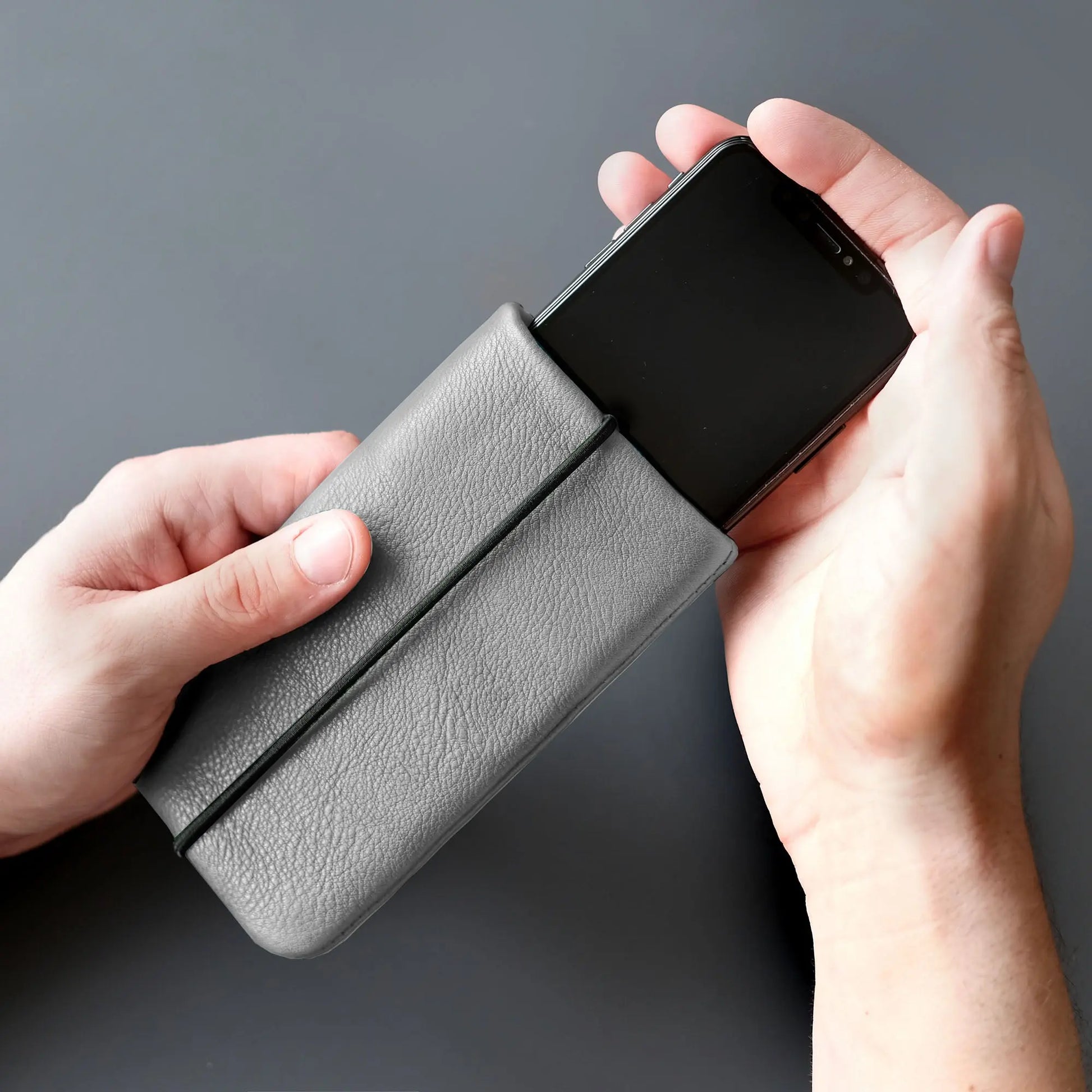 iPhone wird mit zwei Händen in graue Lederhülle geschoben