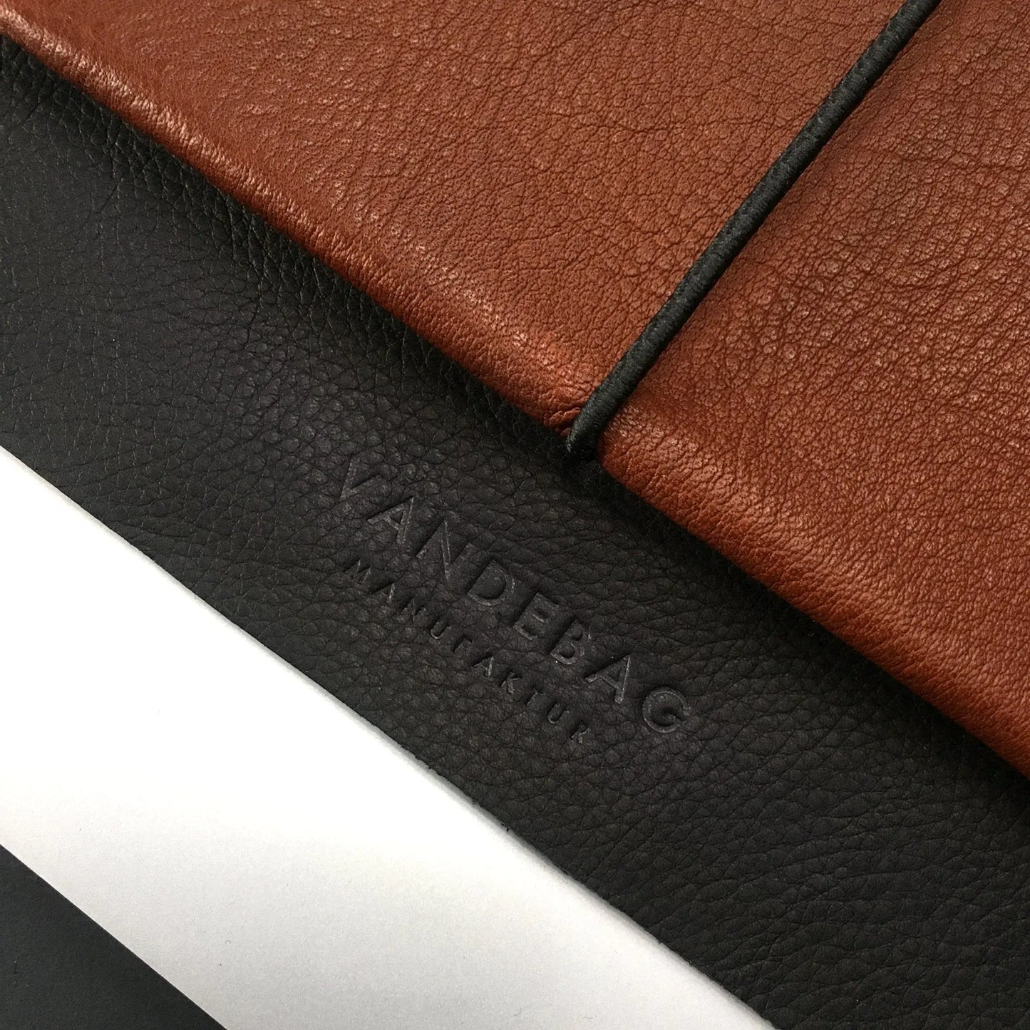 Detail einer braunen Macbookhülle aus Leder mit schwarzer Verschlussklappe in die das Logo eingeprägt ist