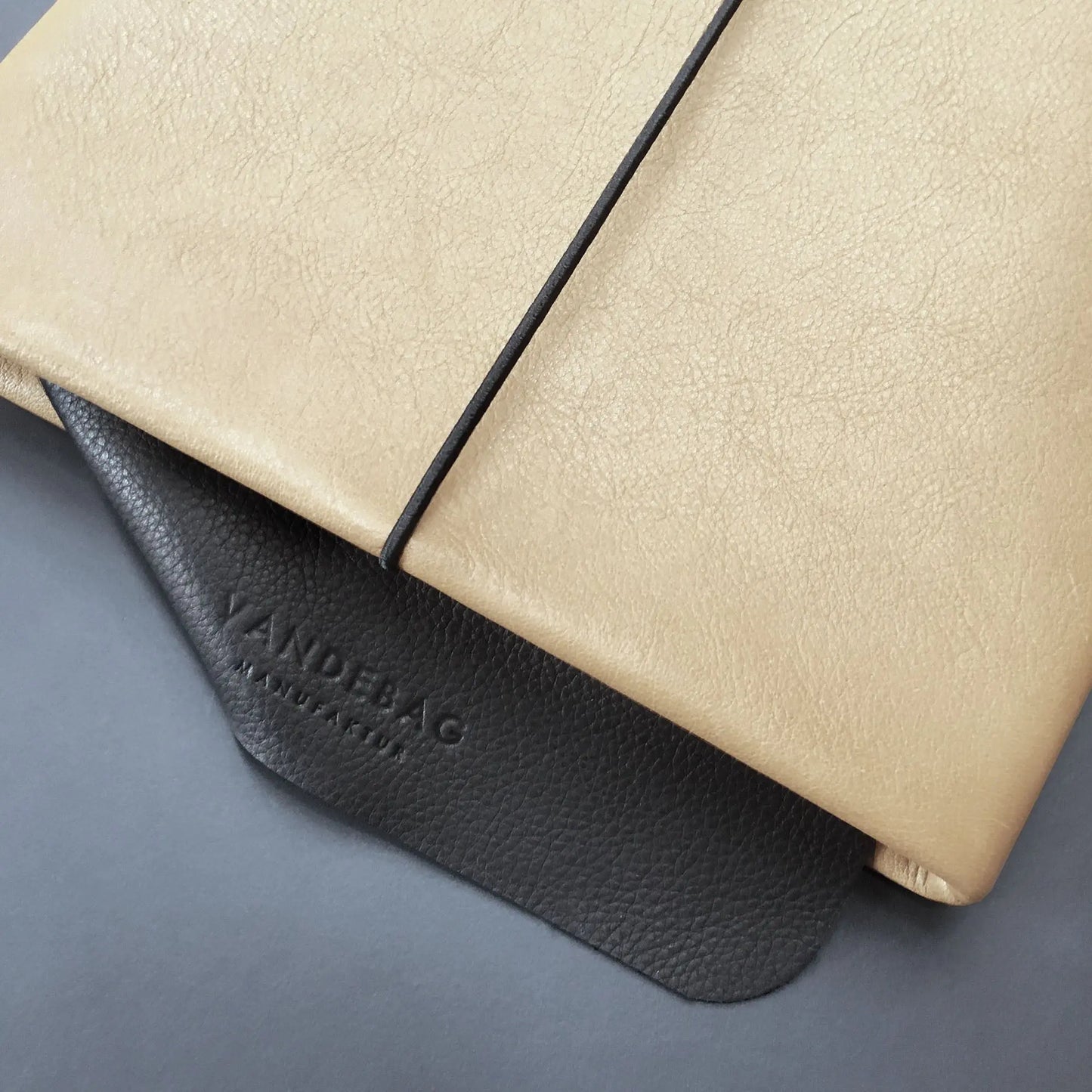 sandfarbene iPad Hülle aus Rindsleder mit Verschlussgummi und schwarzer Lederklappe in die "VANDEBAG Manufaktur" eingeprägt ist.