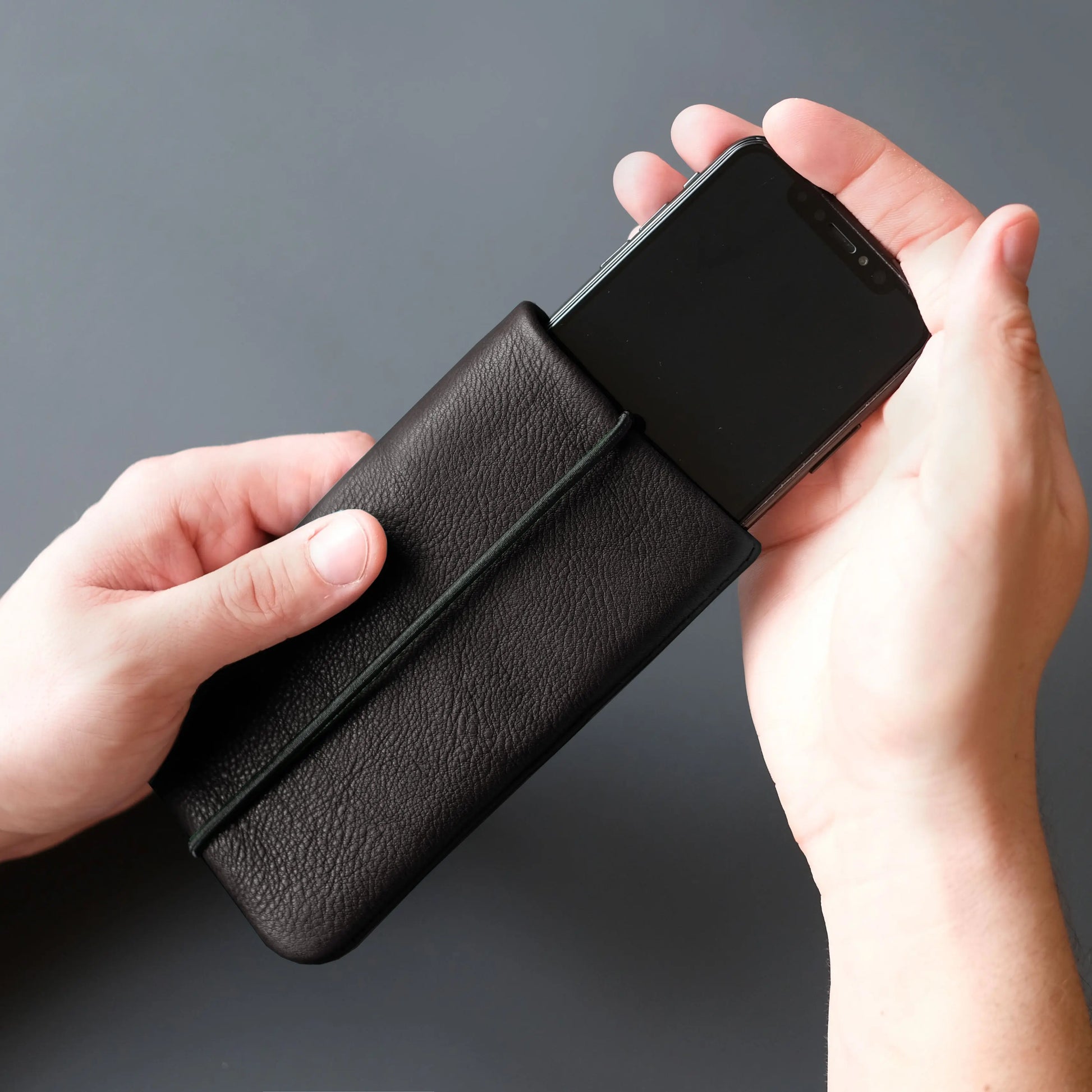 iPhone-Hülle aus schwarzem Leder in die mit zwei Händen ein Smartphone geschoben wird