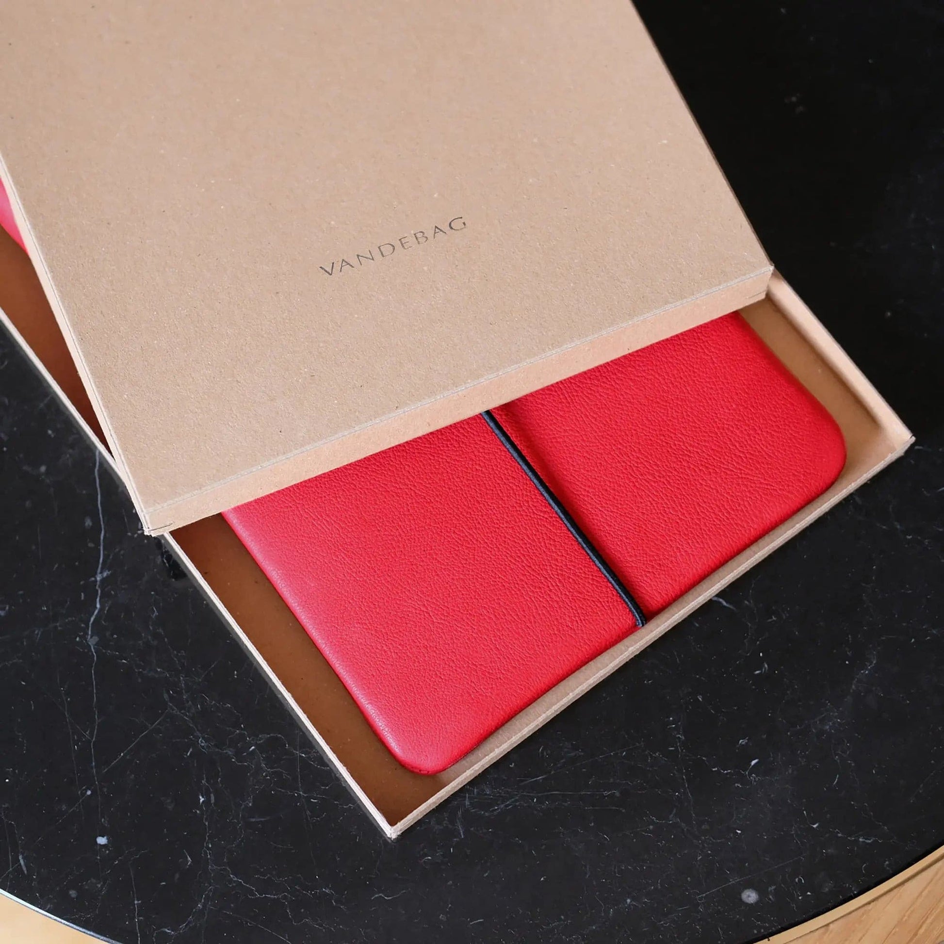 Macbookhülle aus rotem Leder liegt in einem Geschenkkarton mit Aufdruck Vandebag