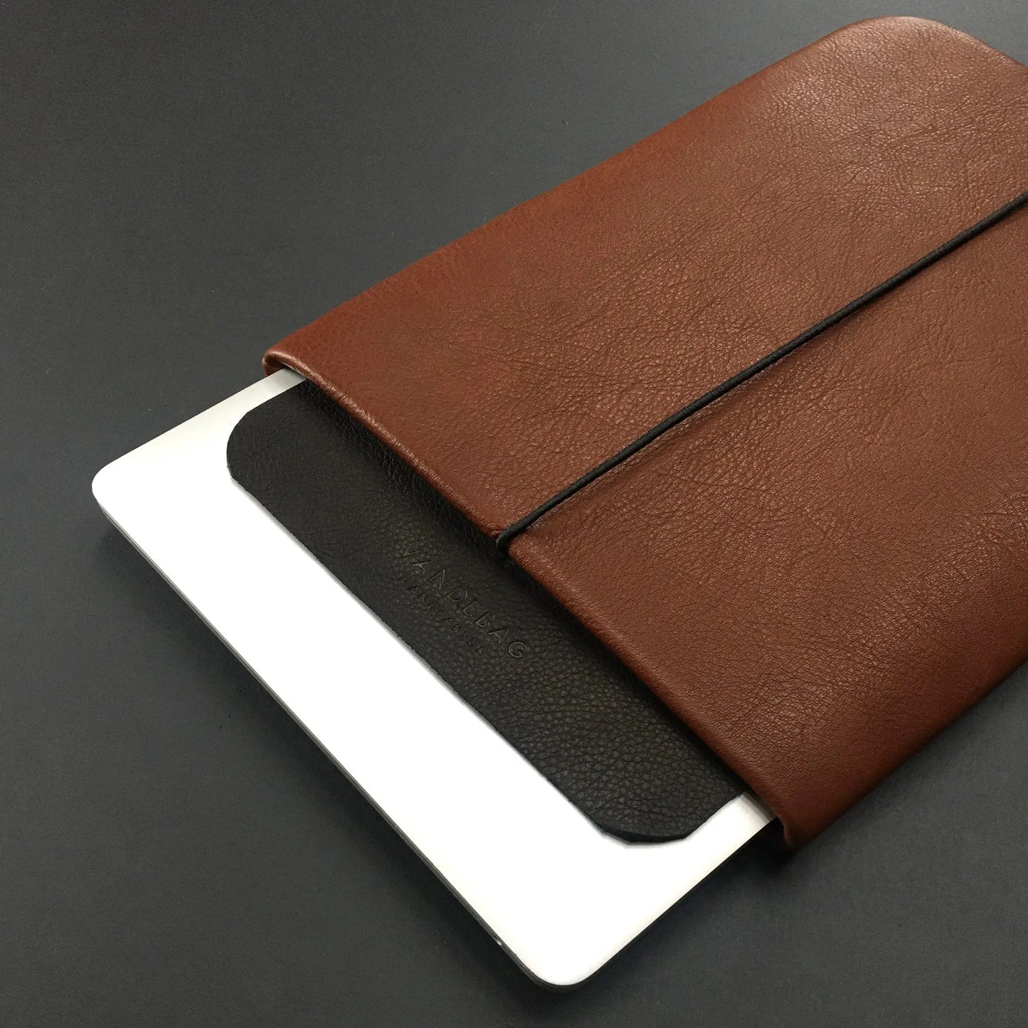Notebookhülle aus braunem Leder mit schwarzer Verschlussklappe und mit Macbook 