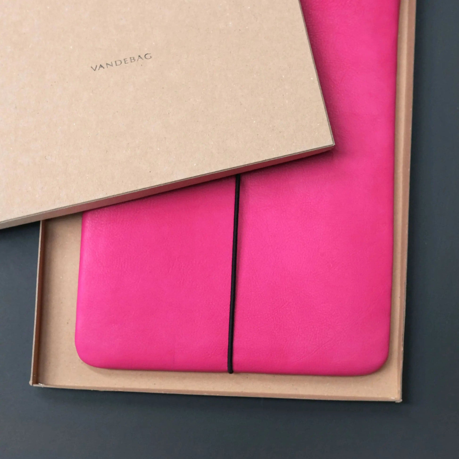 Macbookhülle aus pinkem Leder liegt in einer Produkbox mit der Aufschrift VANDEBAG
