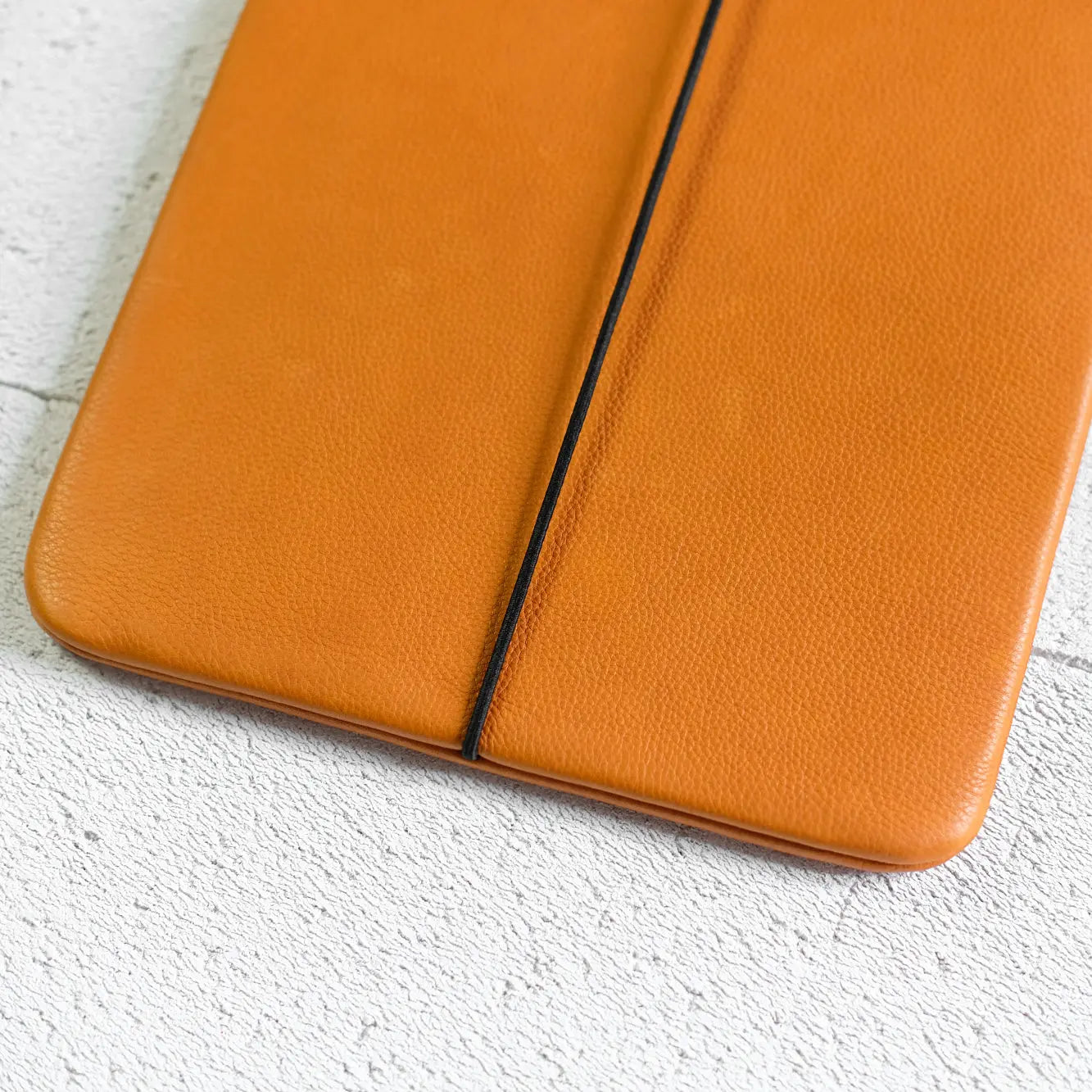 iPadhülle aus orangefarbenem Leder mit leichter Narbung und schwarzem Verschlussgummi