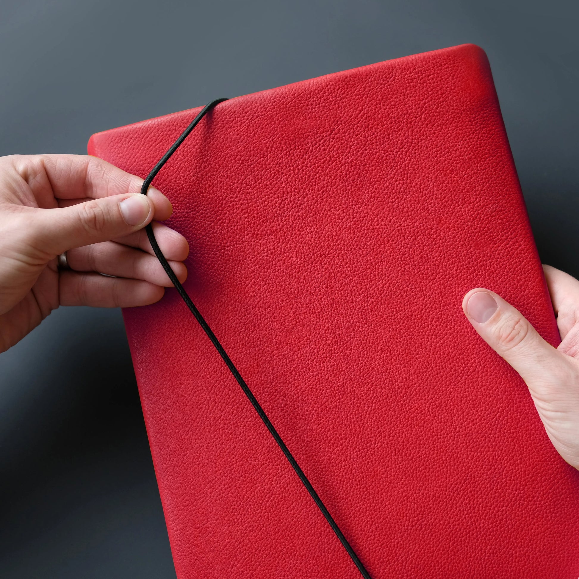 schwarzer Verschlussgummi wird um rote Macbook Hülle aus Leder gezogen