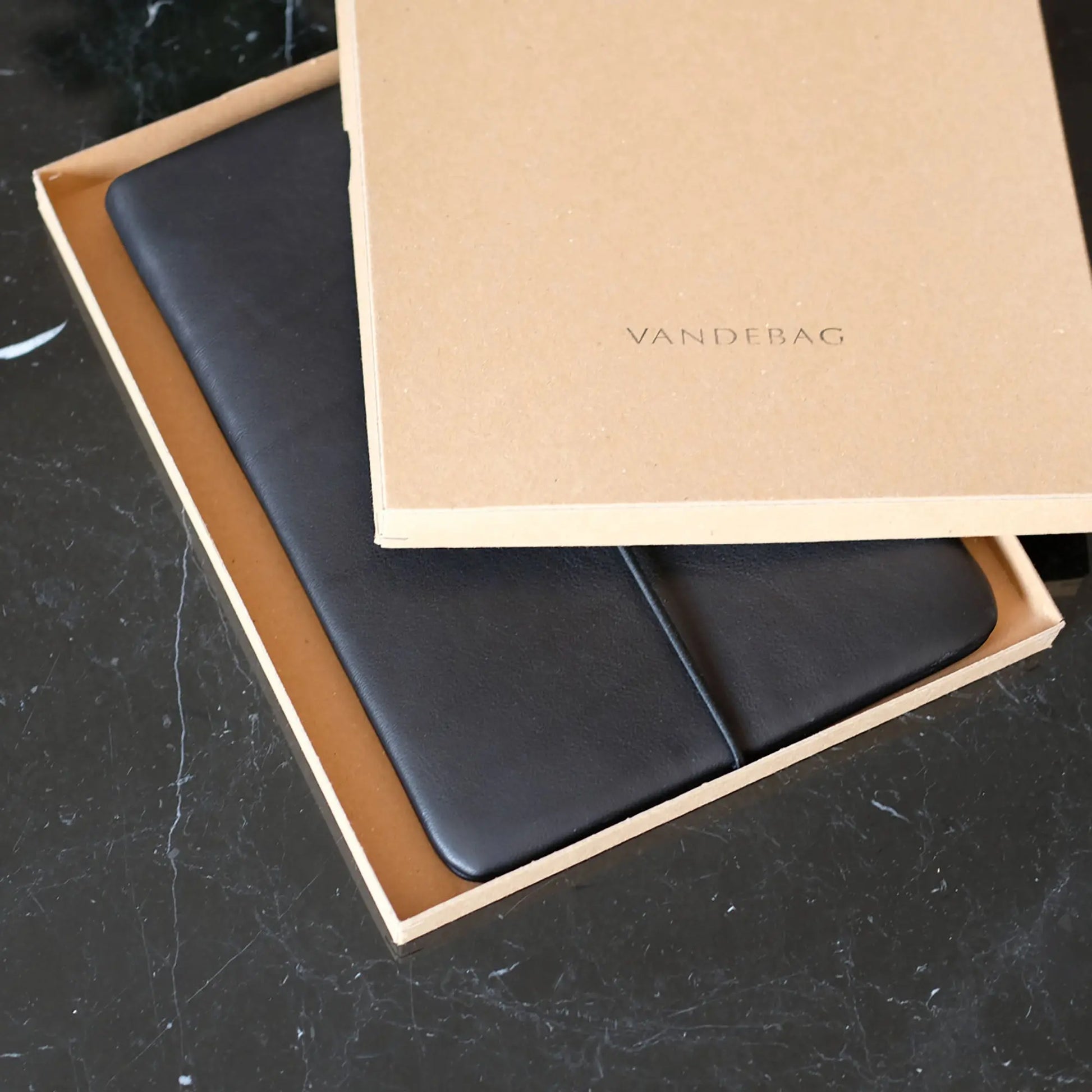 schwarze Lederhülle für iPads liegt in einem Geschenkkarton auf einem schwarzen Tisch